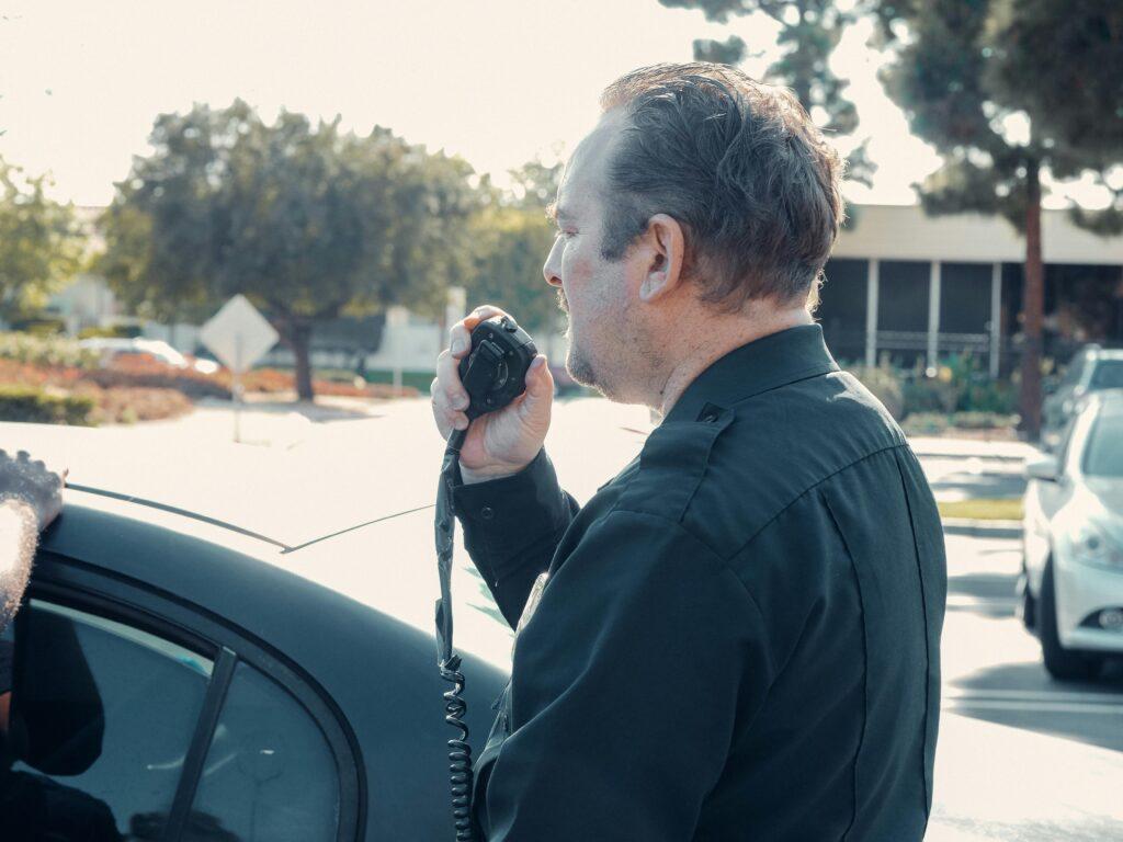 A police officer communicates using a radio outdoors during daytime patrol.